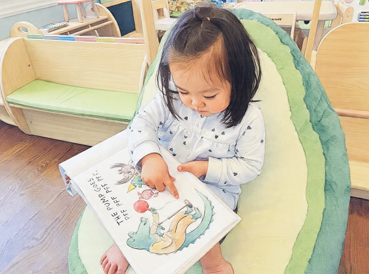 A young child reading a picture book in the Ivy Grove playroom